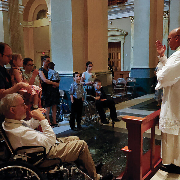 A Norbertine priest blesses two people in wheelchairs from the Nunes family. A Norbertine priest blesses two people in wheelchairs from the Nunes family.