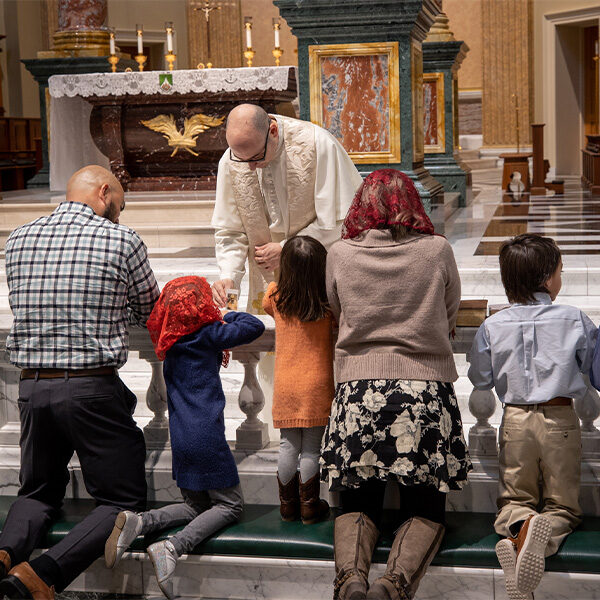 A Norbertine Priest in the Shrine Church holds a relic for the Morales Family to venerate as they kneel at the communion rail and ask for healing. A Norbertine Priest in the Shrine Church holds a relic for the Morales Family to venerate as they kneel at the communion rail and ask for healing.