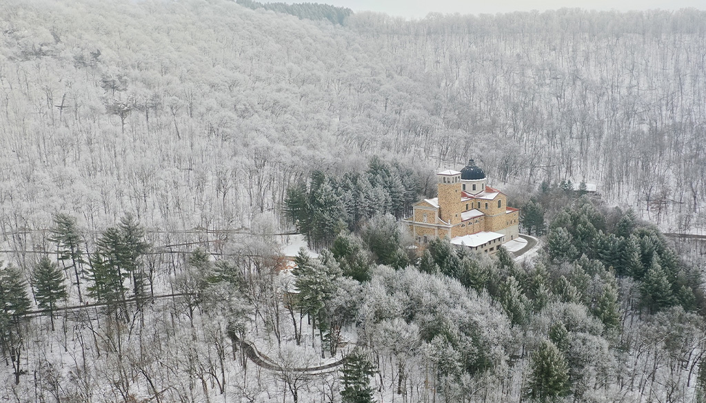 An aerial view of the Shrine of Our Lady of Guadalupe surrounded by bluffs and trees covered in snow during winter in La Crosse, Wisconsin.
