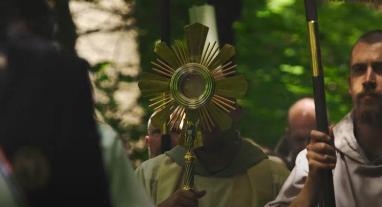 A religious procession at the Shrine of Our Lady of Guadalupe in La Crosse, Wisconsin, featuring a cleric holding a golden monstrance during a sacred Eucharistic ritual, as part of a video titled 'Holy Eucharist: Jesus Fulfills His Promise' by Father Paul Check on June 18, 2024.